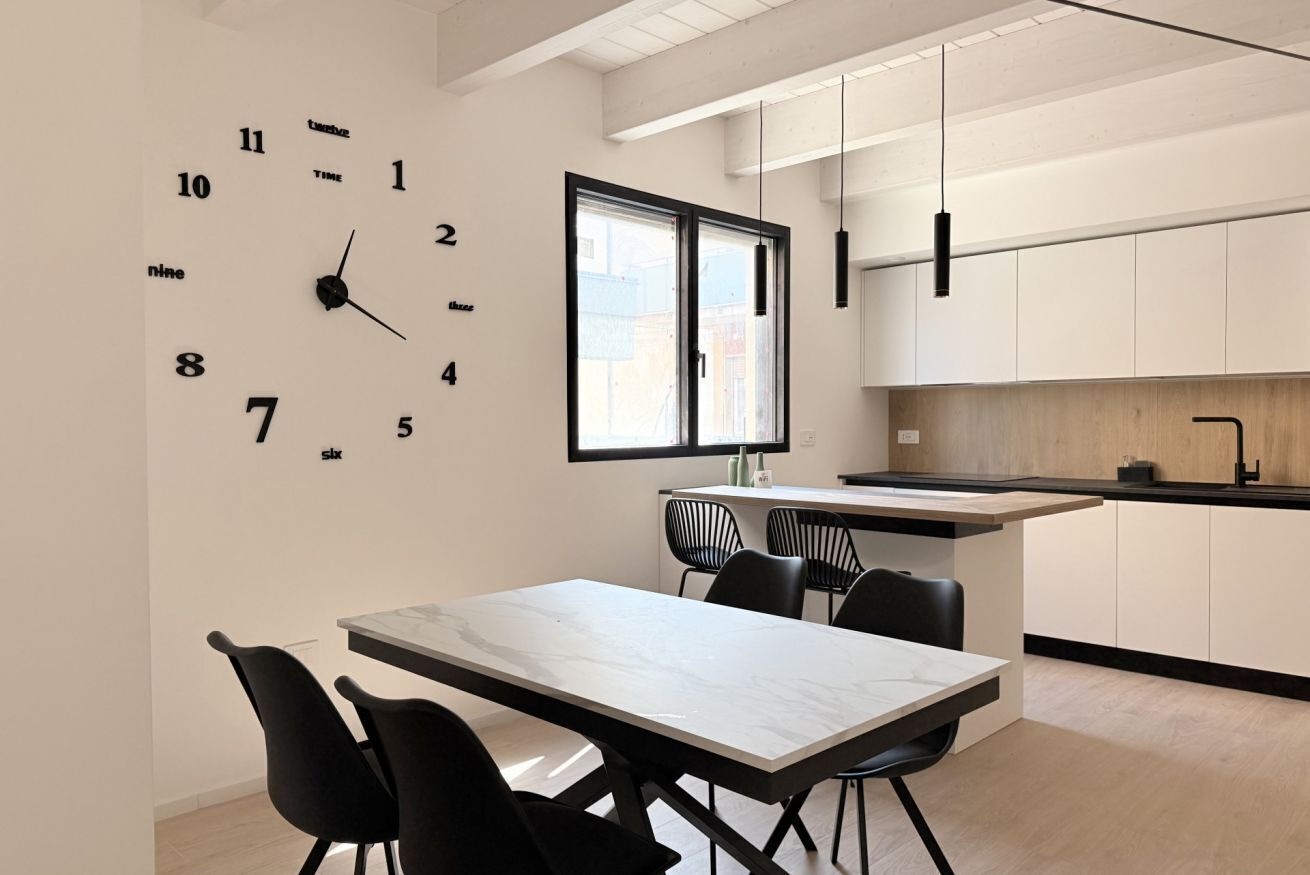 A modern kitchen with a marble countertop, black chairs, and a large wall clock.
