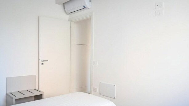 Ein schlicht eingerichtetes Schlafzimmer mit einem Einzelbett, einem Nachttisch und einer Tür.