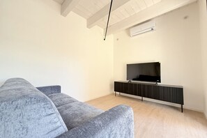 A modern living room with a grey sofa, a black entertainment unit, and a mounted television. - SE310 – Senigallia, stylish apartment with air conditioning, private garage and outdoor courtyard (Senigallia)