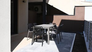 Eine Außenpatio mit Tisch und Stühlen, einem überdachten Bereich und einem Gebäudeeingang.