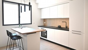 Eine moderne Küche mit weißen Schränken, einer schwarzen Arbeitsplatte und einem eingebauten Ofen. Es gibt eine kleine Kücheninsel mit einem Barhocker und ein Fenster über der Spüle.