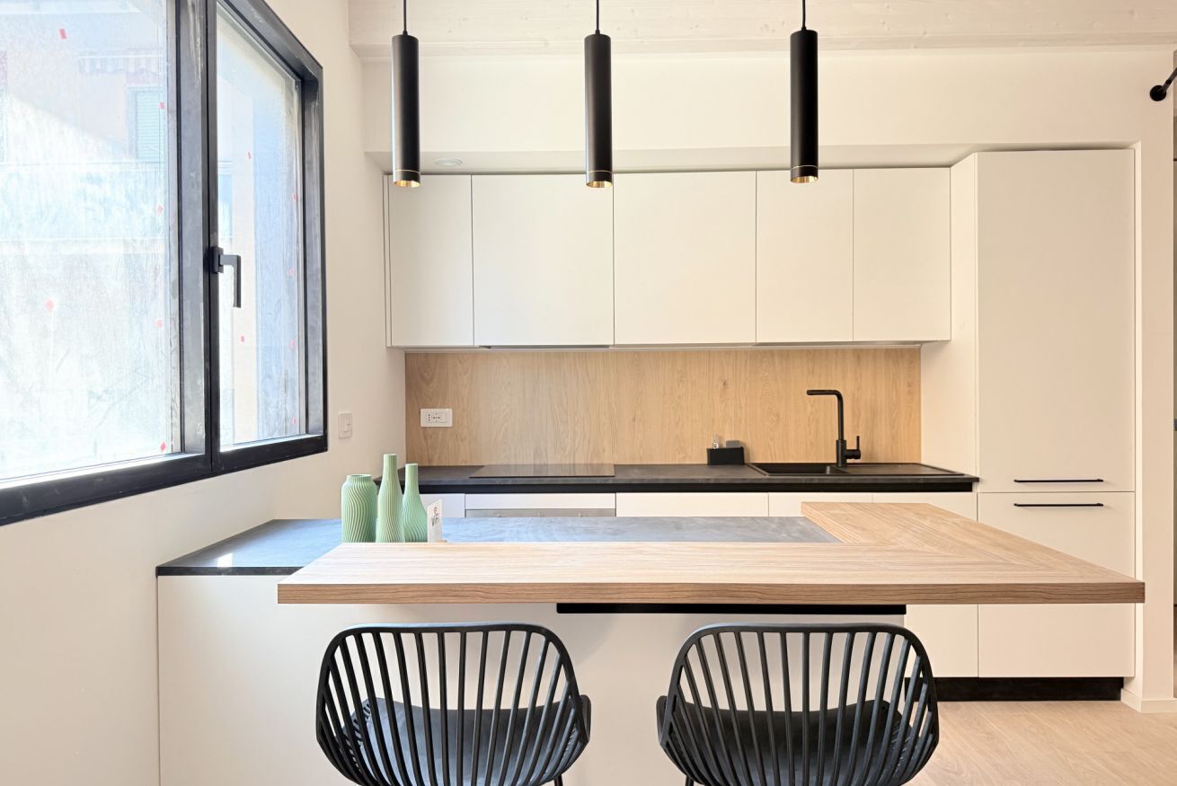 A modern kitchen with a central island, black chairs, and pendant lighting.