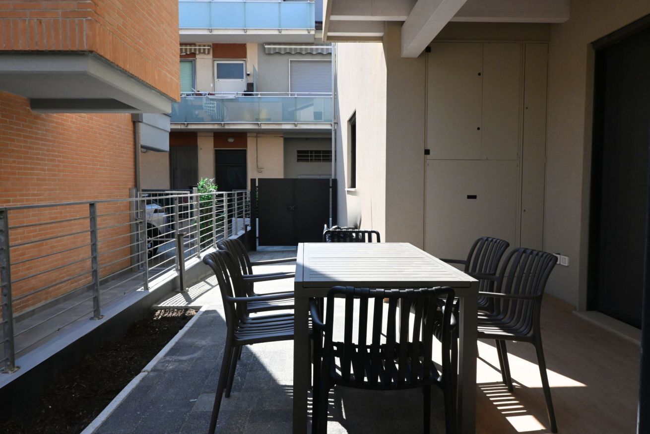 An outdoor patio with a table and chairs, a metal railing, and a building in the background.
