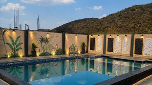 A swimming pool with steps leading up to it, surrounded by a wall with decorative panels and plants. - The Art of Field (Udaipur)