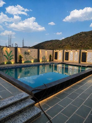 A swimming pool with steps leading up to it, surrounded by a wall with decorative panels and plants. - The Art of Field (Udaipur)