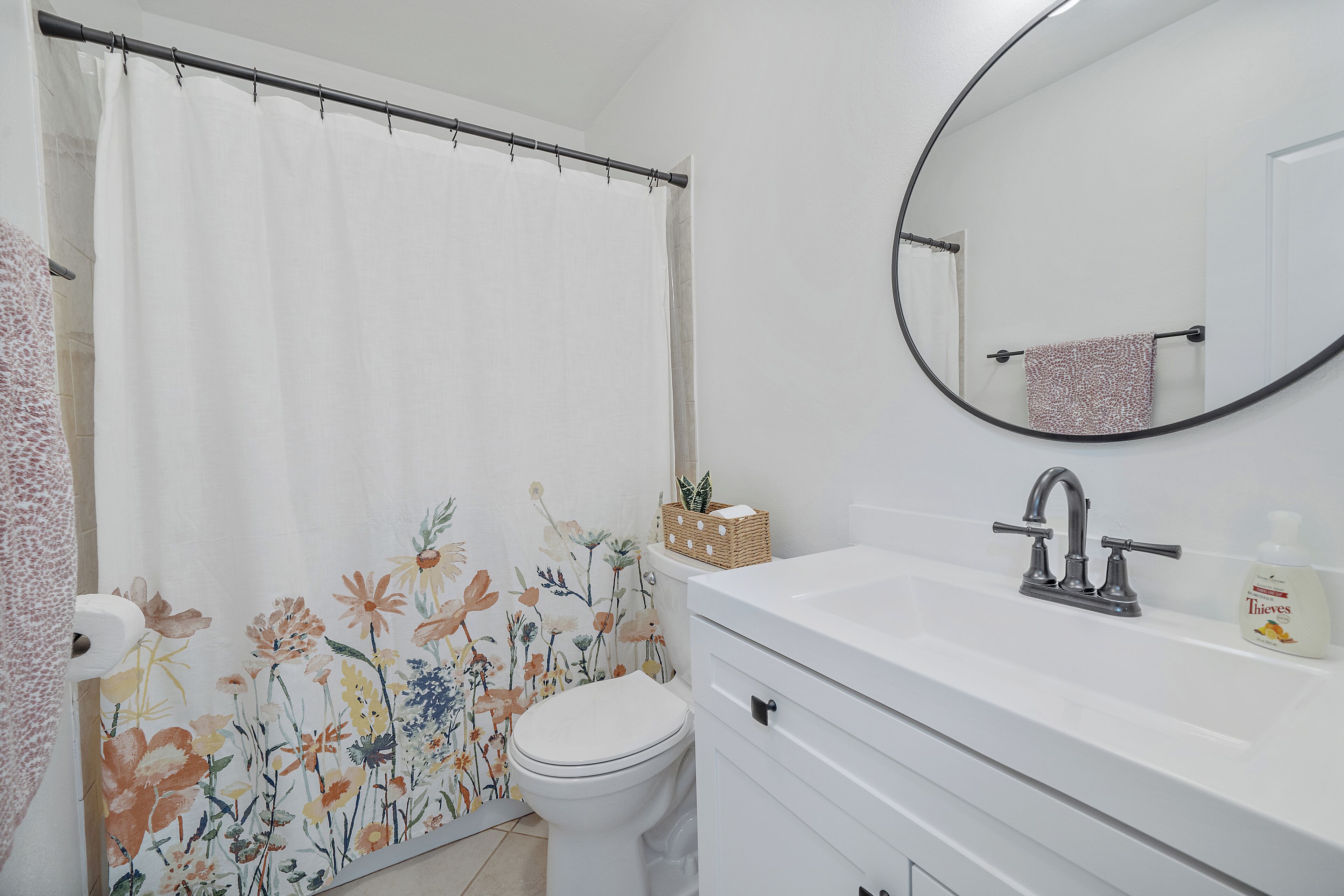 Een badkamer met douchegordijn, toilet, wastafel en spiegel.