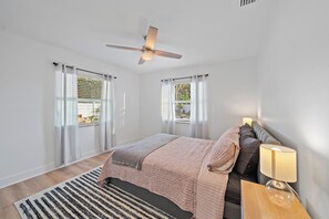 A bedroom with a bed, a nightstand, a lamp, a ceiling fan, and two windows with curtains. - Memory‑Making Sarasota Stay with Heated Pool, Spa & Modern Comfort (Sarasota)