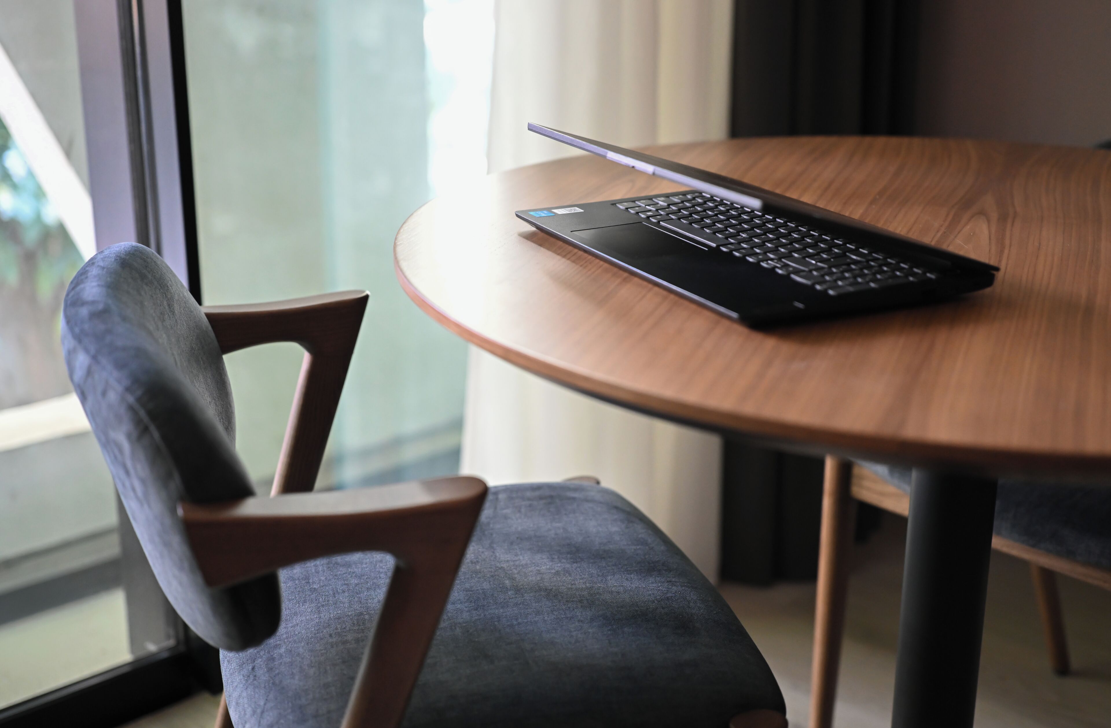 Ein Laptop auf einem runden Holztisch, daneben ein Stuhl.