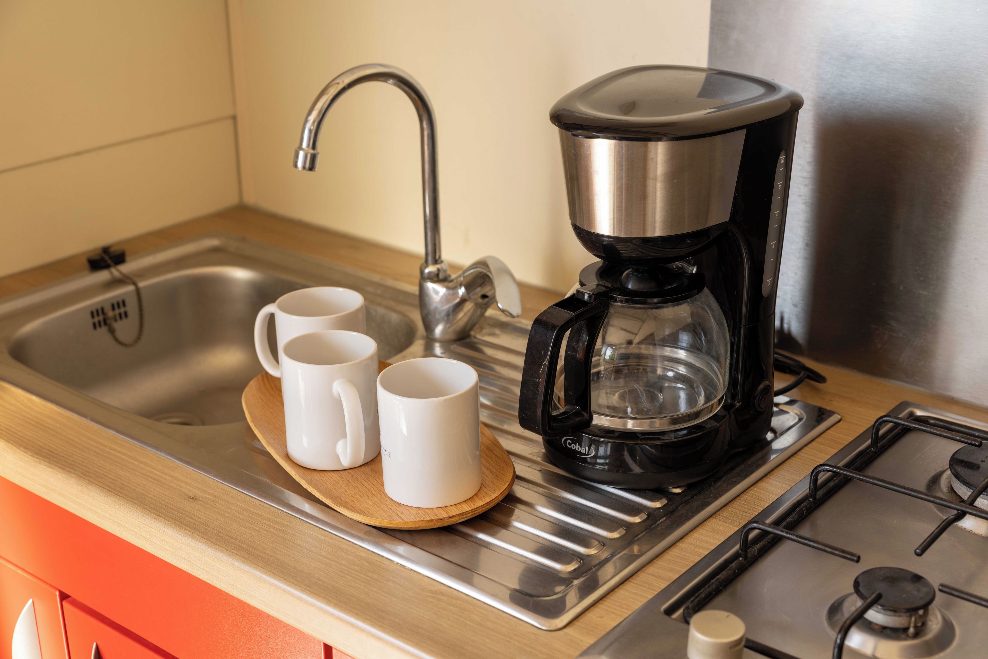 Eine Küche mit Kaffeemaschine, zwei weißen Tassen und einem Edelstahl-Spülbecken.