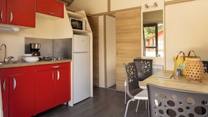 A compact kitchen with red cabinets, a white refrigerator, a microwave, and a stove. There is a dining area with a table, chairs, and a window with a view of the outside. - Family Cottage (Saint-Thibault-des-Vignes)