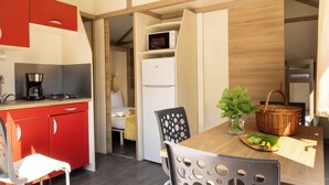 A compact kitchenette with a coffee maker, a microwave, and a refrigerator. There is a dining area with a table, chairs, and a basket with fruits. - Family Cottage (Saint-Thibault-des-Vignes)