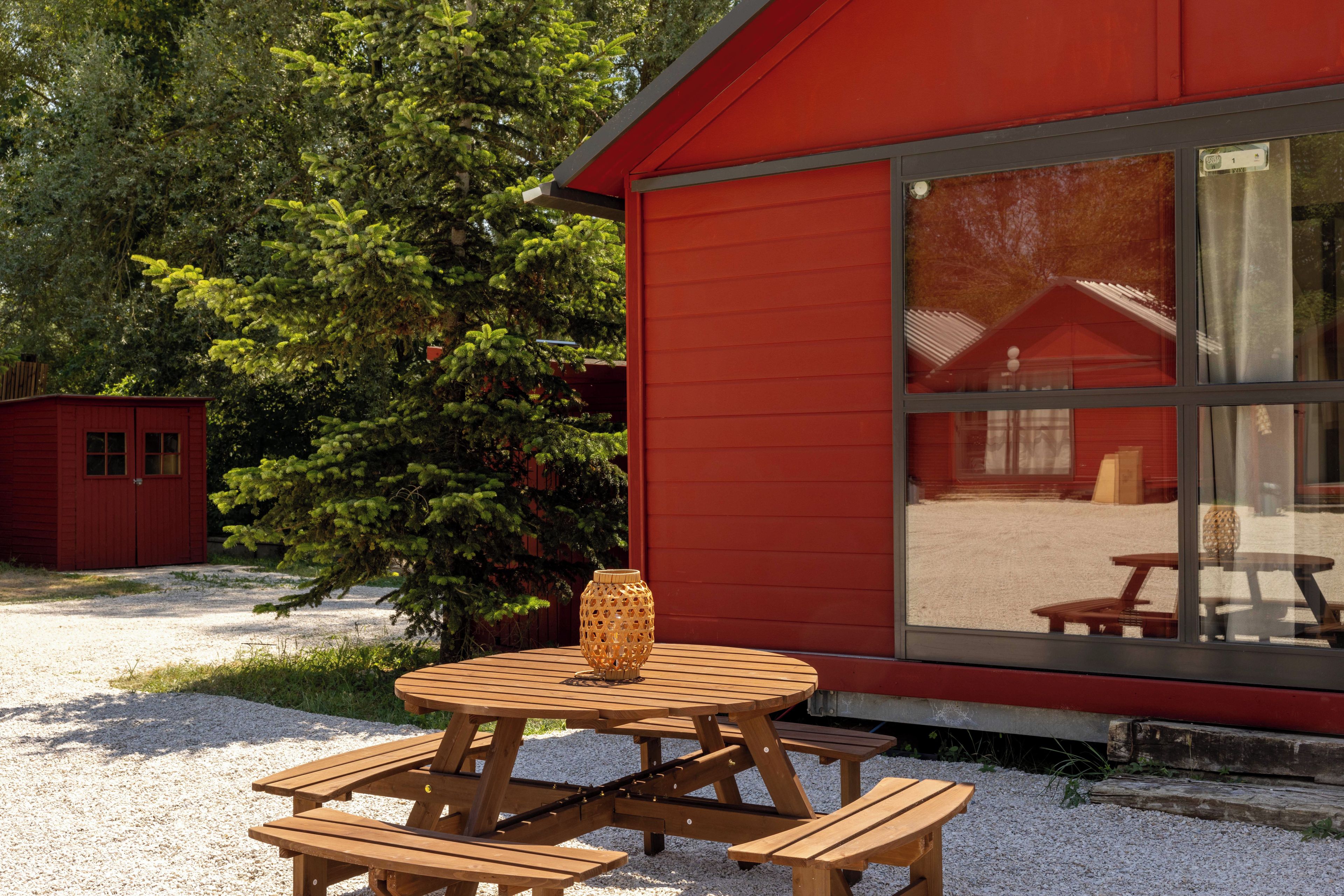 A red building with a large window and a picnic table with benches in front.