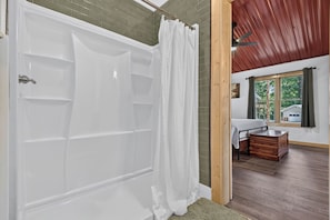 A bathroom with a white bathtub, a shower curtain, and a wooden floor. -  Tucker's Hideaway (Morganton)