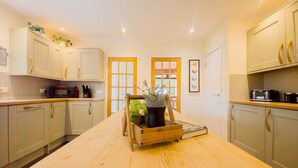 A kitchen with a central wooden table, cabinets, a microwave, and a potted plant. - Kinloch Lodge - Highland hot tub lodge close to Loch Ness (Drumnadrochit)