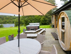 A wooden deck with outdoor furniture, a hot tub, and a view of a lake. - Kinloch Lodge - Highland hot tub lodge close to Loch Ness (Drumnadrochit)