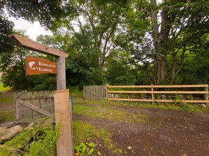 A wooden sign for Kinloch Lodge with a wooden fence and trees in the background. - Kinloch Lodge - Highland hot tub lodge close to Loch Ness (Drumnadrochit)