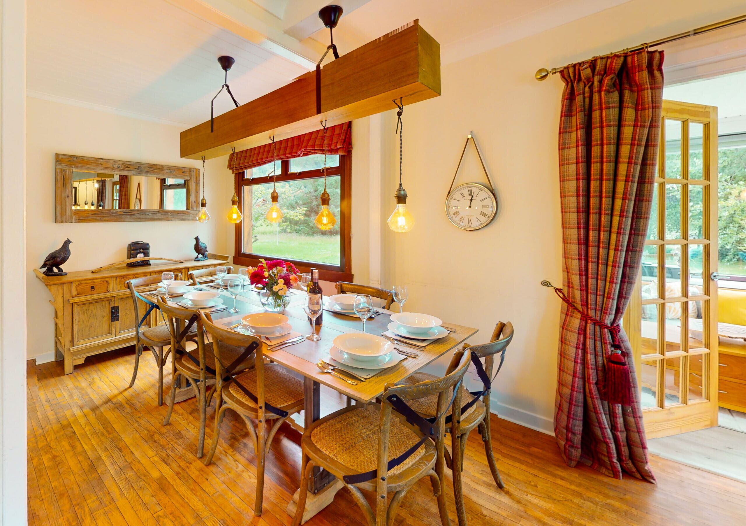 A dining room with a wooden table set for four, surrounded by wicker chairs, a wooden cabinet, and a mirror on the wall.