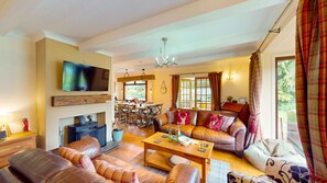 A cozy living room with a fireplace, leather sofas, a dining area with a table and chairs, and a television mounted on the wall. - Kinloch Lodge - Highland hot tub lodge close to Loch Ness (Drumnadrochit)