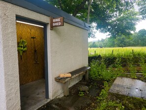 A bike shed with a wooden door, a bench outside, and a rural landscape in the background. - Kinloch Lodge - Highland hot tub lodge close to Loch Ness (Drumnadrochit)