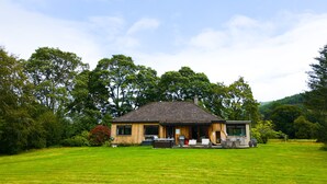 A wooden house with a sloped roof, a front porch, and a lawn in front. - Kinloch Lodge - Highland hot tub lodge close to Loch Ness (Drumnadrochit)