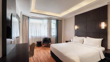 A hotel room with a large bed, a desk, a chair, a TV, and a window with curtains.