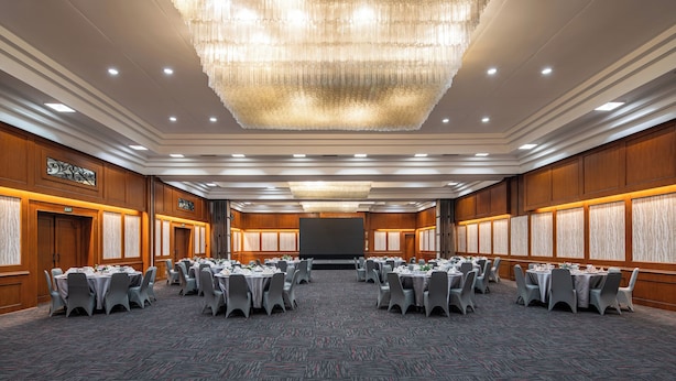 A conference room with round tables, a large chandelier, and a screen at the front. - Bentani Hotel & Residences (North Cirebon)
