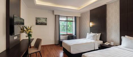 A hotel room with two beds, a desk, a chair, a TV, and a window with curtains.