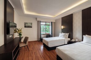 A hotel room with two beds, a desk, a chair, a TV, and a window with curtains.