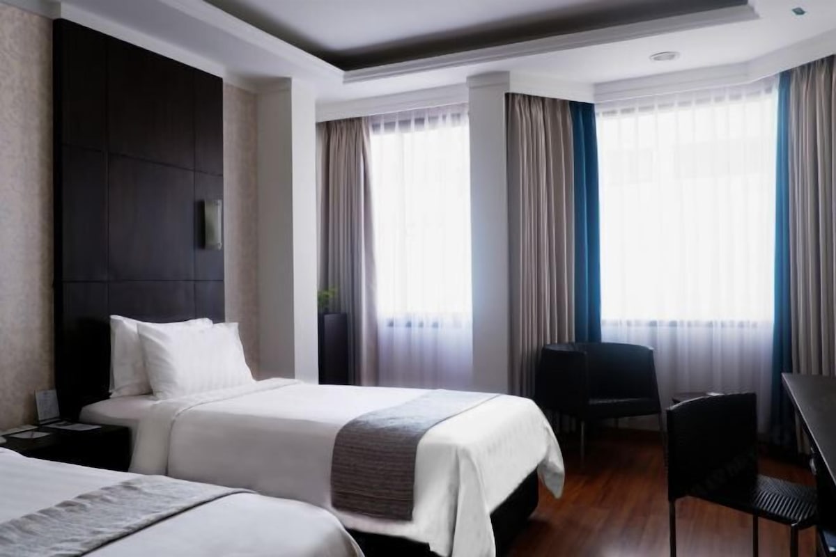 Quarto de hotel com duas camas, uma escrivaninha e uma cadeira.