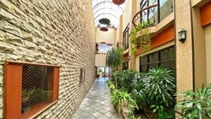A narrow corridor with a stone wall on one side and a balcony with plants on the other. - Bentani Hotel & Residences (North Cirebon)