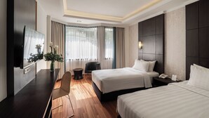 A hotel room with two beds, a desk, a chair, a TV, and a window with curtains. - Bentani Hotel & Residences (North Cirebon)