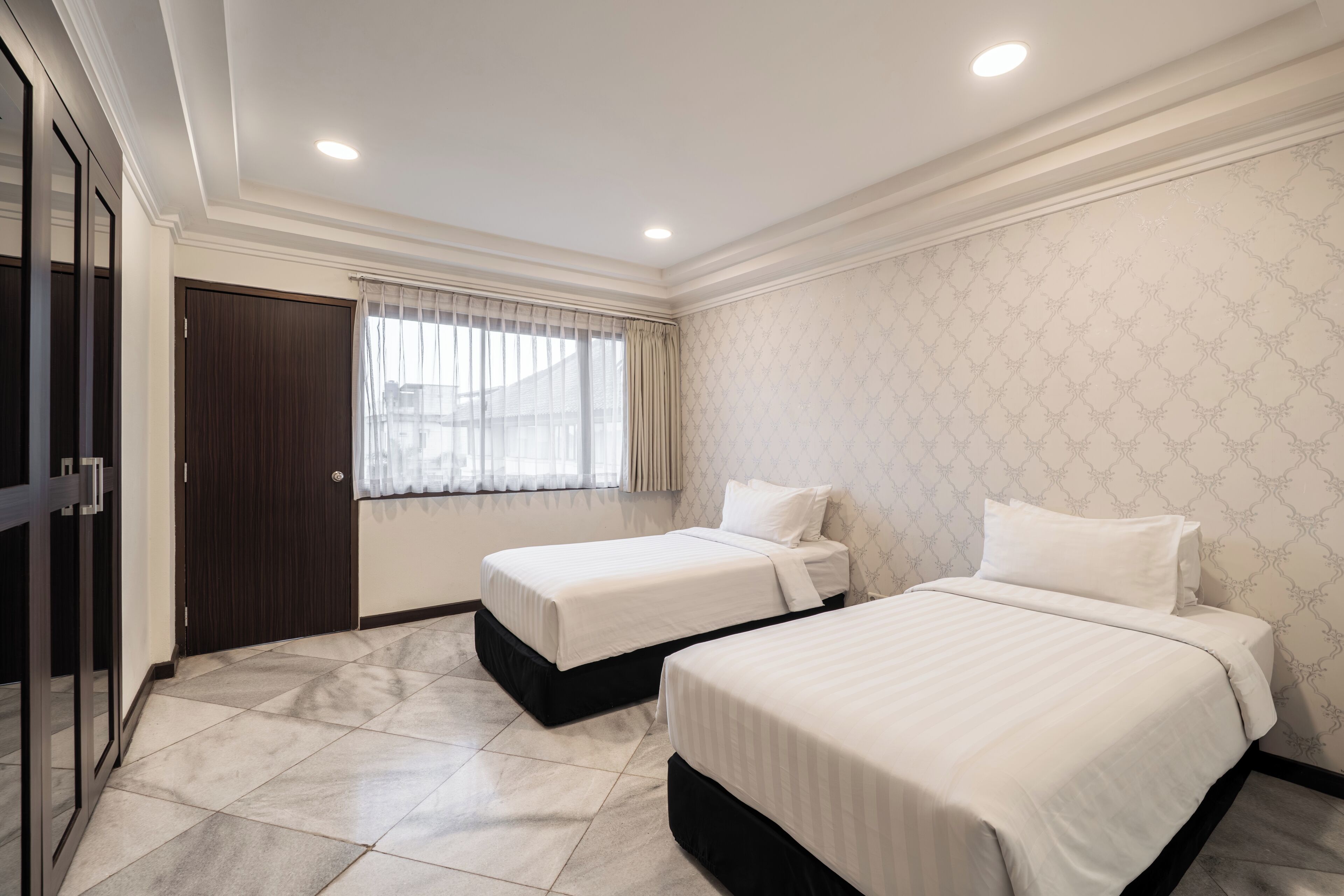 Quarto de hotel com duas camas, uma janela com cortinas, uma porta e parede estampada.