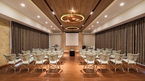 A conference room with a wooden floor, rows of wicker chairs, a large screen, and a podium. - Bentani Hotel & Residences (North Cirebon)