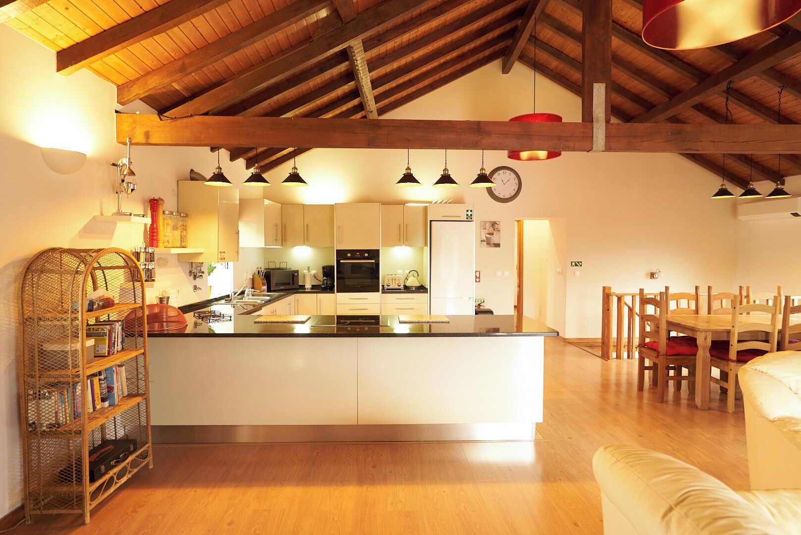 A spacious kitchen with a central island, wooden beams on the ceiling, and pendant lighting.