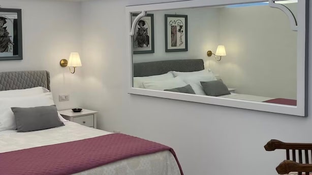 Een hotelkamer met een bed, nachtkastjes, een grote spiegel en wanddecoratie.