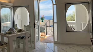 Een kamer met een eettafel, stoelen en uitzicht op zee door grote ramen.