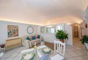 A dining area with a table set for two, a sofa, a mirror, and a potted plant. - Loft 11 in Praiano with Stunning Sea View (Praiano)