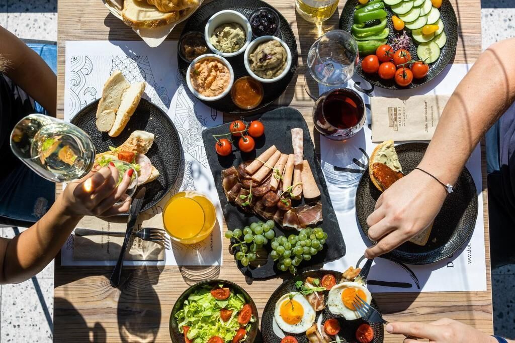 Een gedekte tafel met verschillende soorten eten, zoals brood, vleeswaren, groenten en een glas sinaasappelsap.