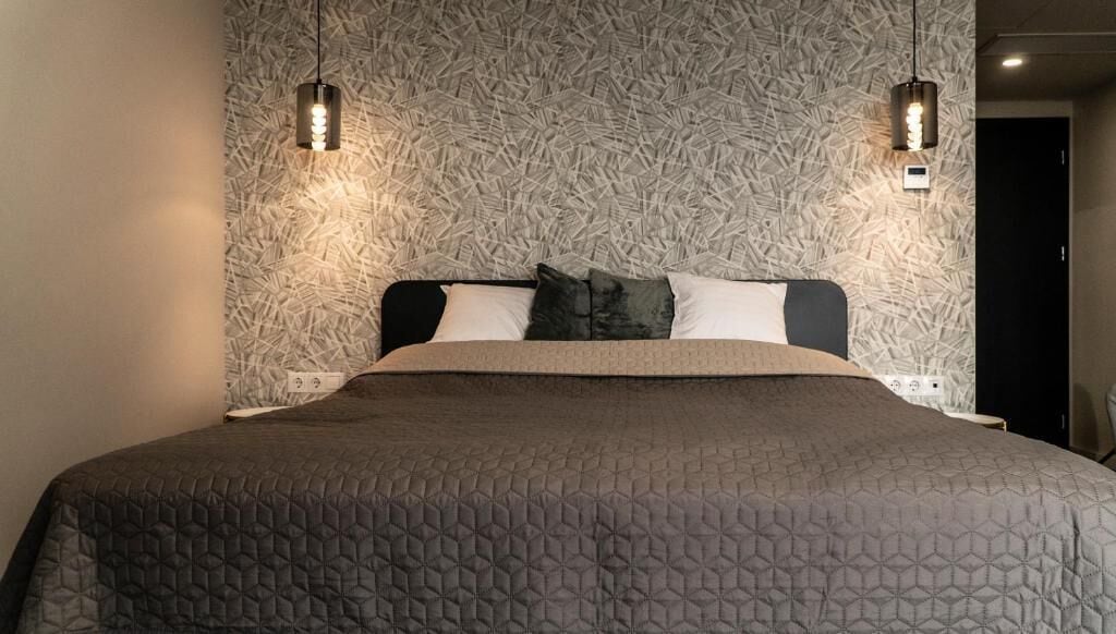 A bed with a geometric patterned bedspread, two wall-mounted light fixtures, and a textured wall behind the bed.