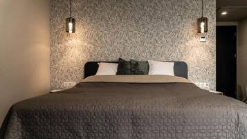 A bed with a geometric patterned bedspread, two wall-mounted light fixtures, and a textured wall behind the bed.