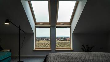 Une chambre avec un puits de lumière, un lit, une lampe sur pied et une vue sur les vignes.