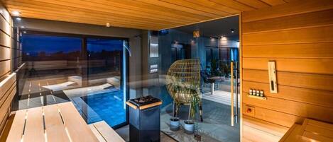 Una sala de sauna con bancos de madera, una pared de vidrio y una silla.