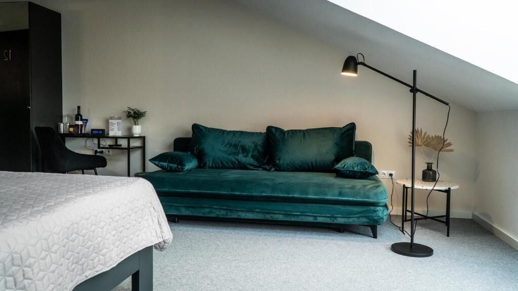 Et værelse med en seng, en grøn sofa, et lille bord med en lampe og en plante.