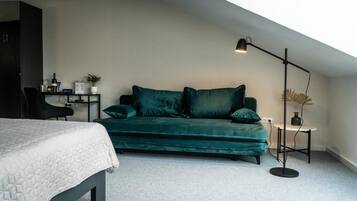 Et værelse med en seng, en grøn sofa, et lille bord med en lampe og en plante.