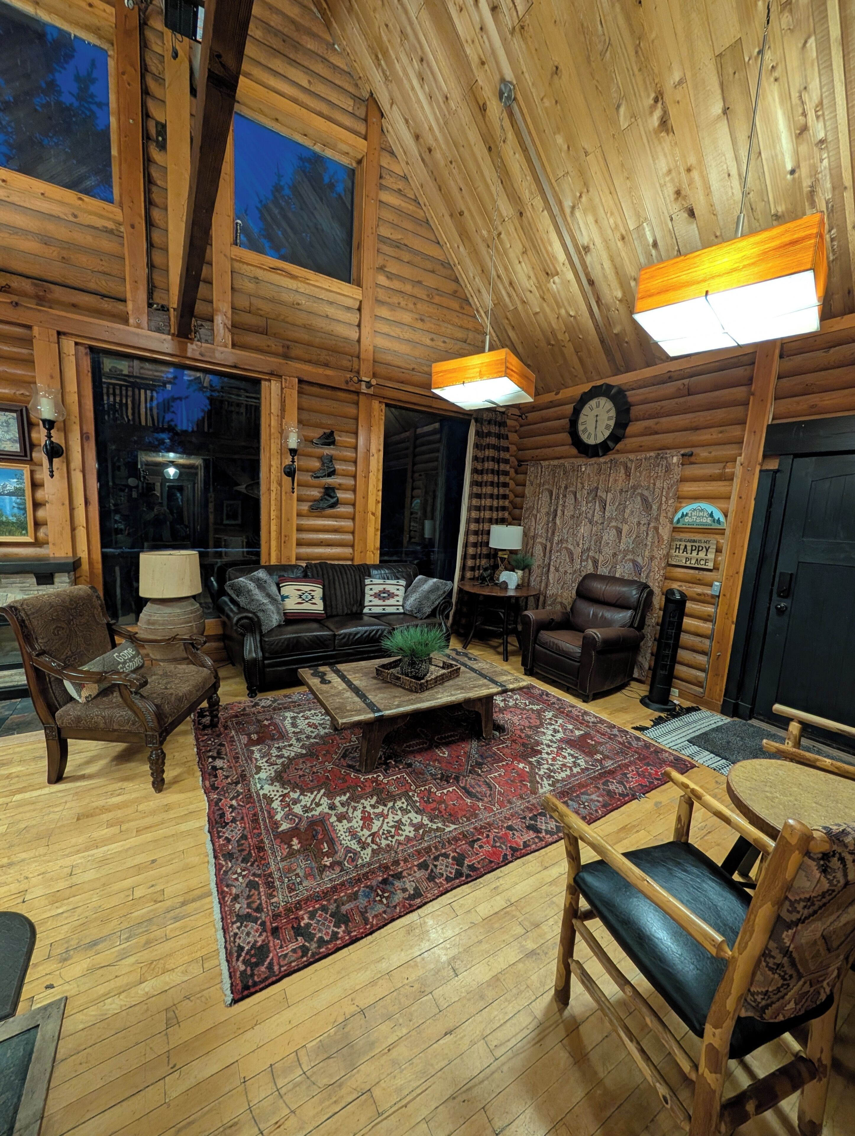 Ein Holzblockhaus-Interieur mit Holzboden, einer Couch, einem Couchtisch, einem Kamin und einem großen Fenster.