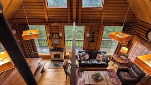 A cozy log cabin interior with a fireplace, leather furniture, and a large window overlooking a forest. - Private Mountain cabin, hot tub, 10 min. to Bozeman  10 min. to Bridger Bowl (Bozeman)