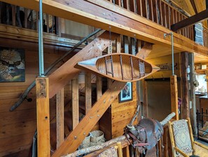 A wooden interior with a staircase, a woven basket, and a saddle.