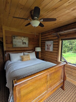 A wooden cabin bedroom with a bed, a ceiling fan, and two framed animal pictures.