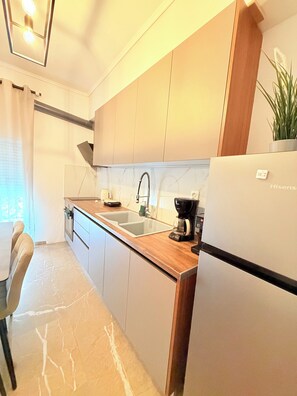 A modern kitchen with a built-in sink, a coffee maker, and a refrigerator. - Cozy 2-bedroom apartment in Thessaloniki with AC near the Metro-family friendly (Thessaloniki)