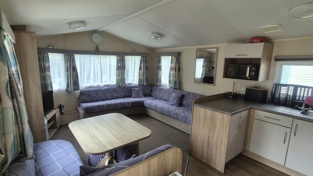 A compact RV interior with a sofa, a dining table, a kitchenette, and a television.